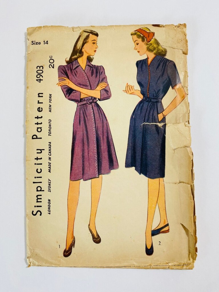 Simplicity dress pattern: two women in shirtdresses are standing facing each other. One has her arms crossed and the other is inspecting her fingernails.